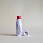 Vely tinted pink lip balm in white cylindrical packaging on a beige background