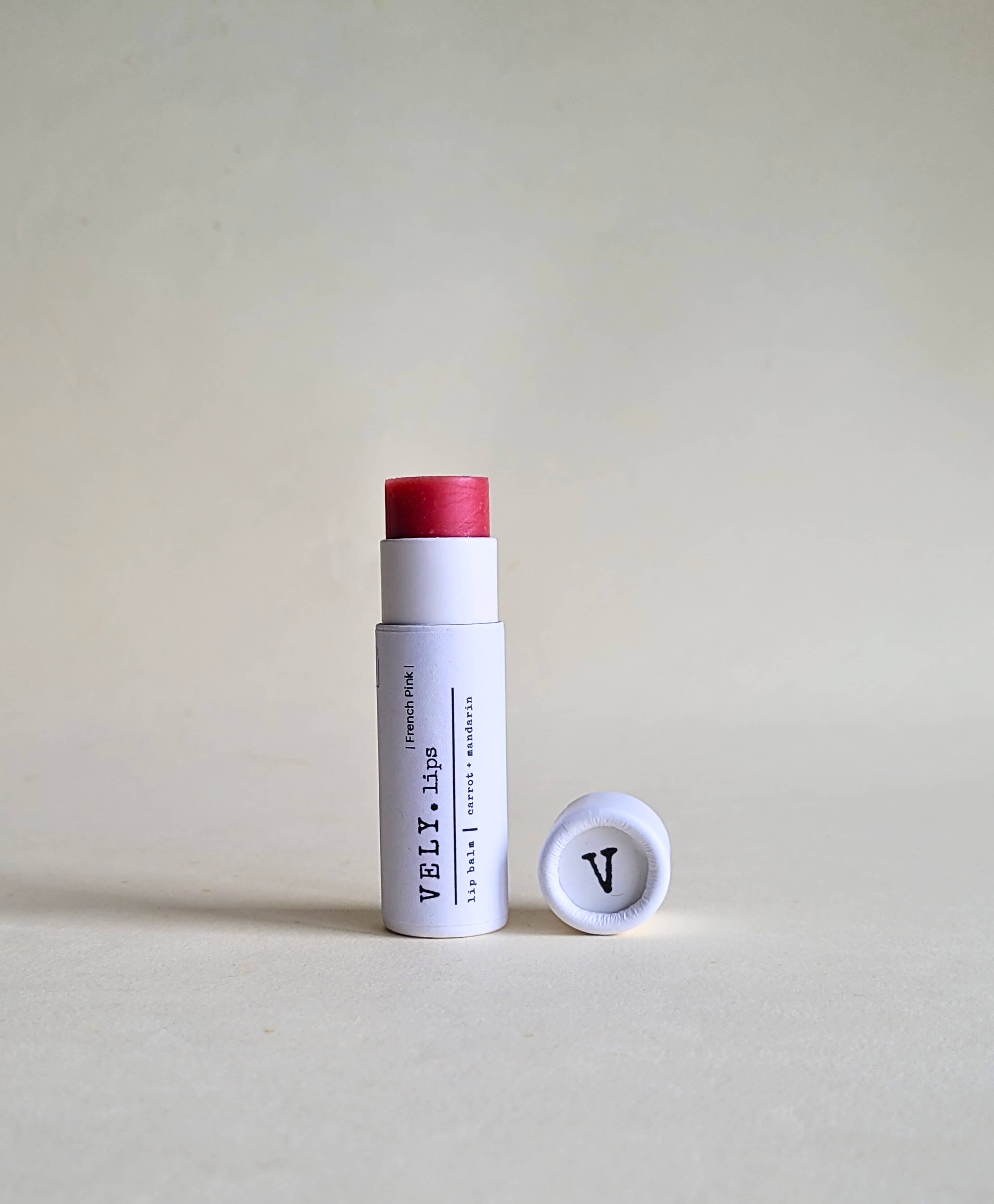 Vely tinted pink lip balm in white cylindrical packaging on a beige background