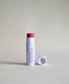 Vely tinted pink lip balm in white cylindrical packaging on a beige background