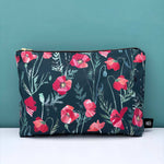 Floral-patterned pouch with red poppy flowers on a dark background against a teal wall.