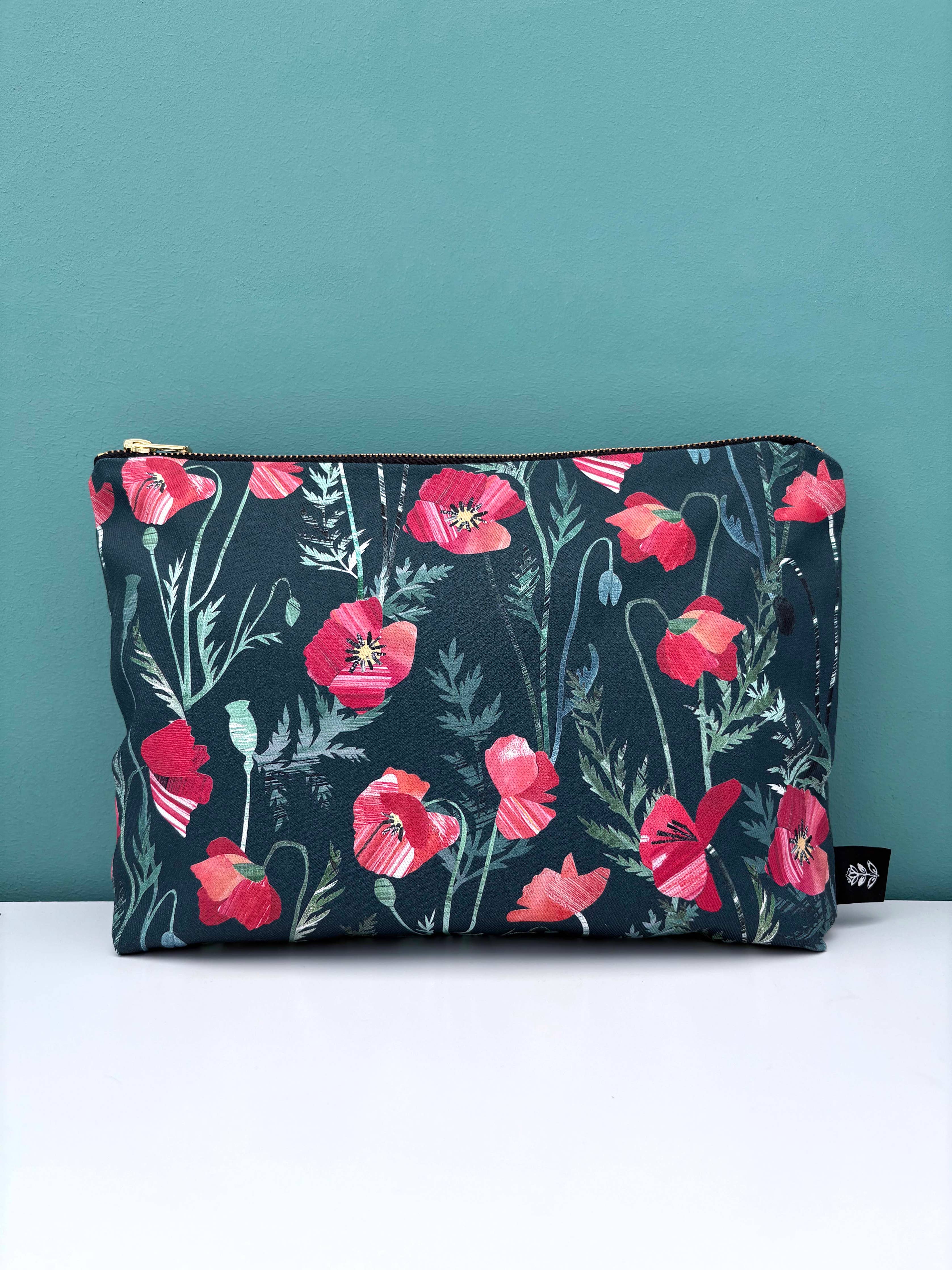Floral-patterned pouch with red poppy flowers on a dark background against a teal wall.