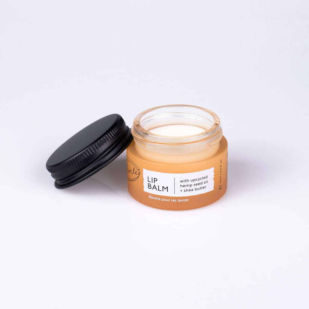 An open UpCircle Lip balm jar with black lid on a white background