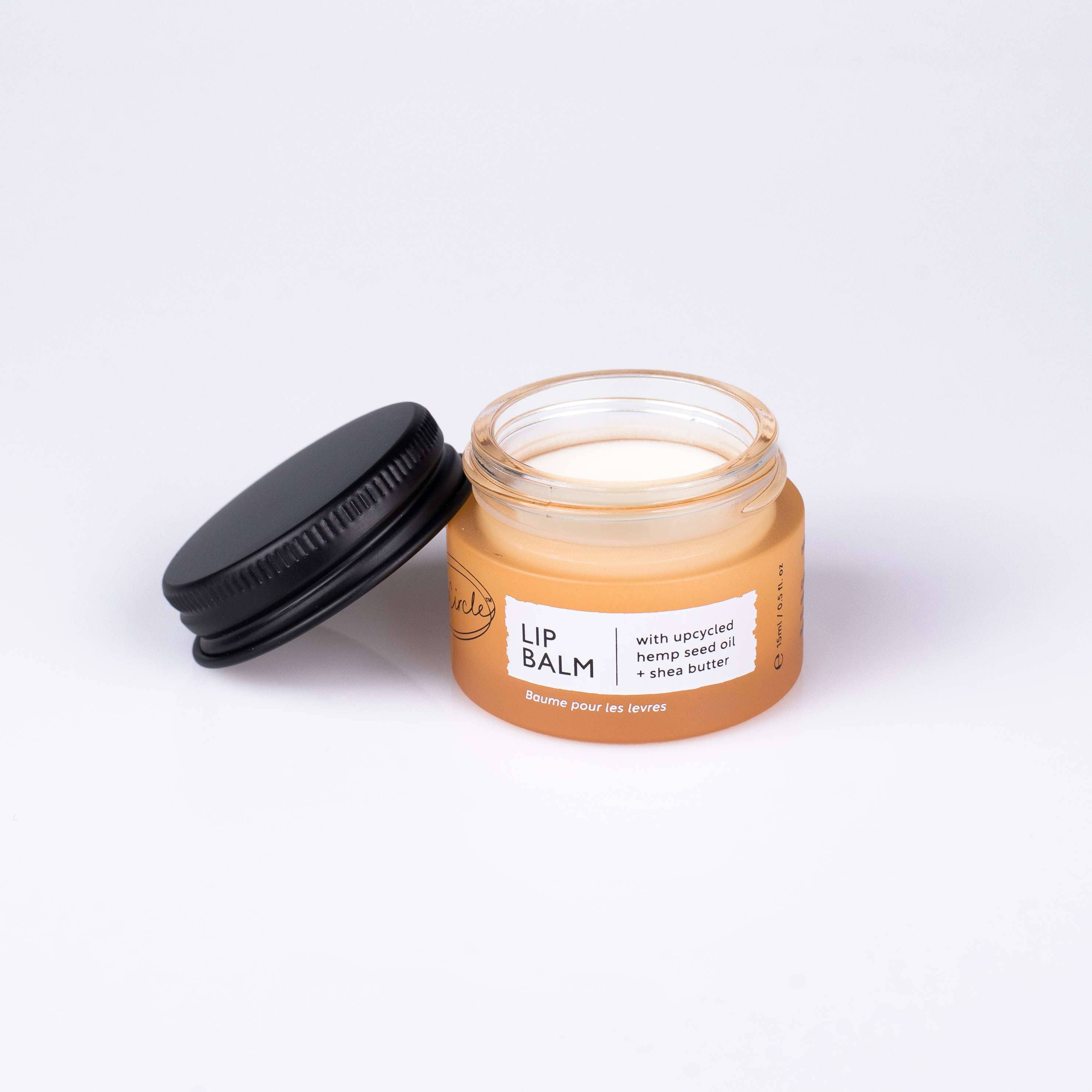 An open UpCircle Lip balm jar with black lid on a white background