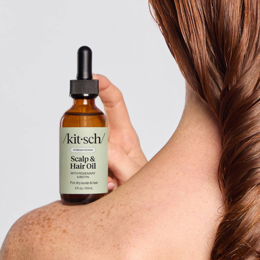 Person holding a bottle of Kitsch scalp and hair oil, with damp hair, with a plain background
