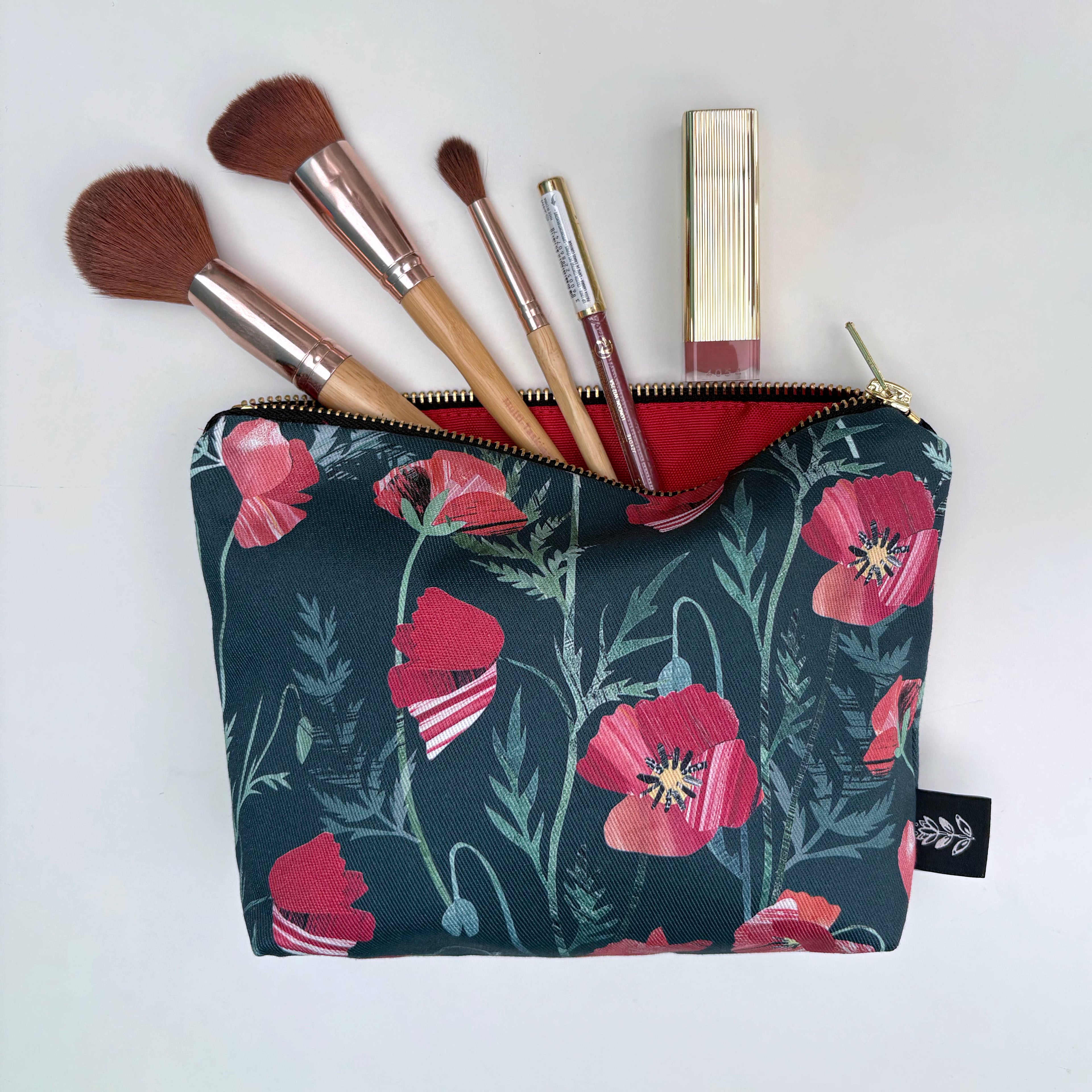 Makeup bag with floral red poppy design containing makeup brushes and lip products on a white background