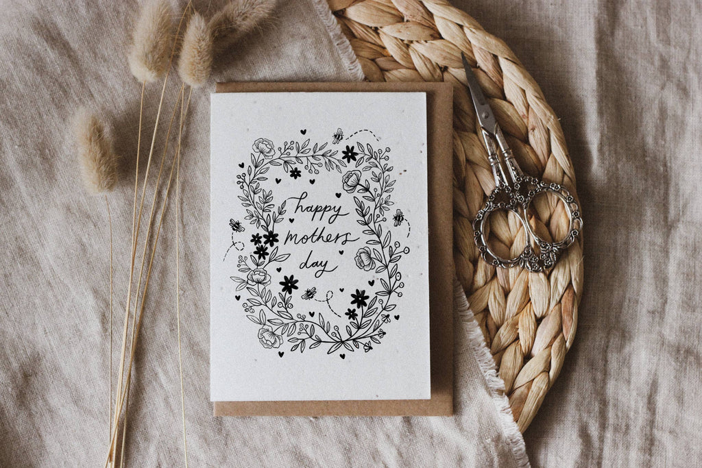 Greeting card with 'Happy Mother's Day' text and floral with bees design on a textured surface with scissors and dried plants.