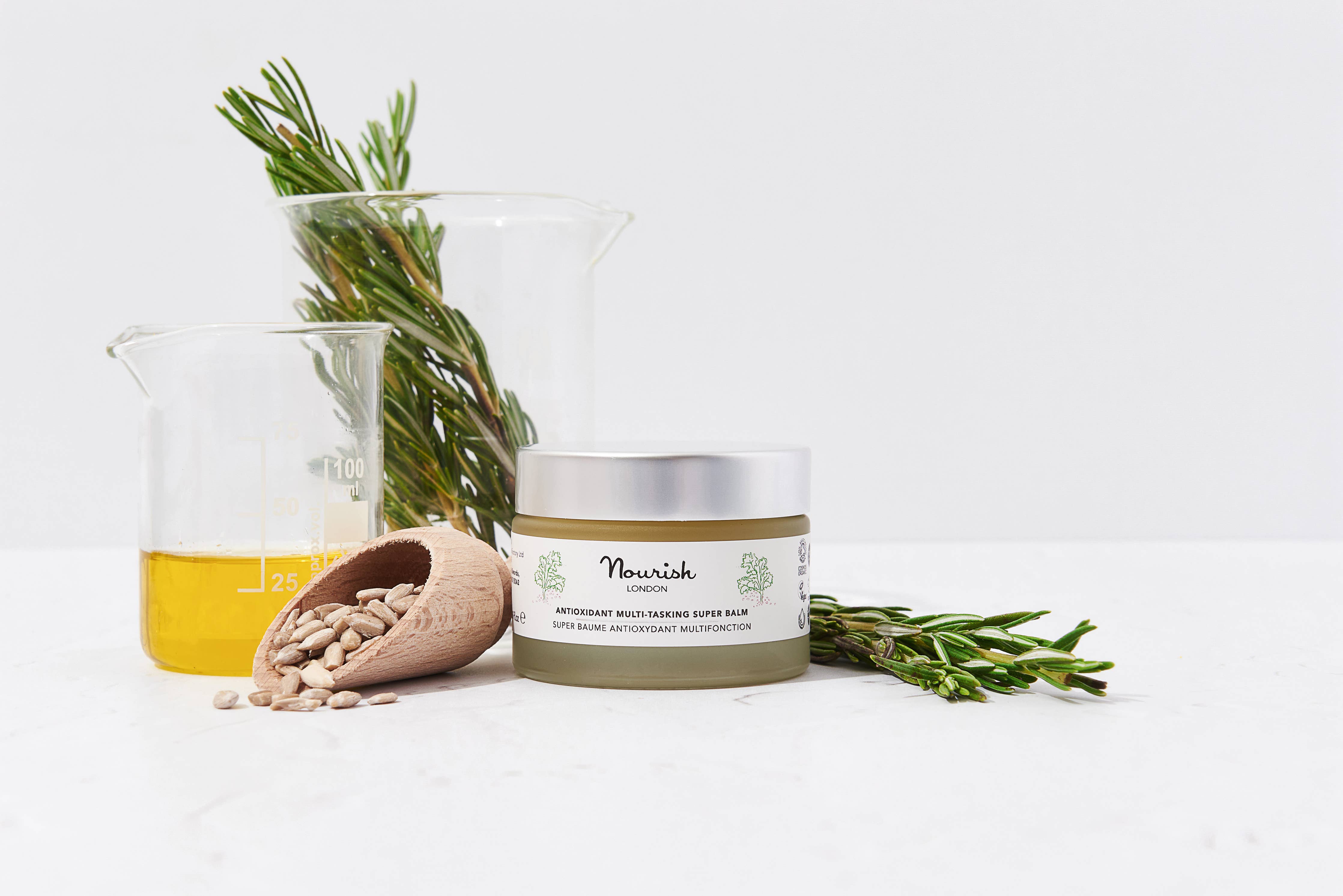 Jar of Nourish product with rosemary and a beaker on a white background