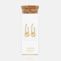 Gold hoop earrings in a clear packaging with cork lid on a white background