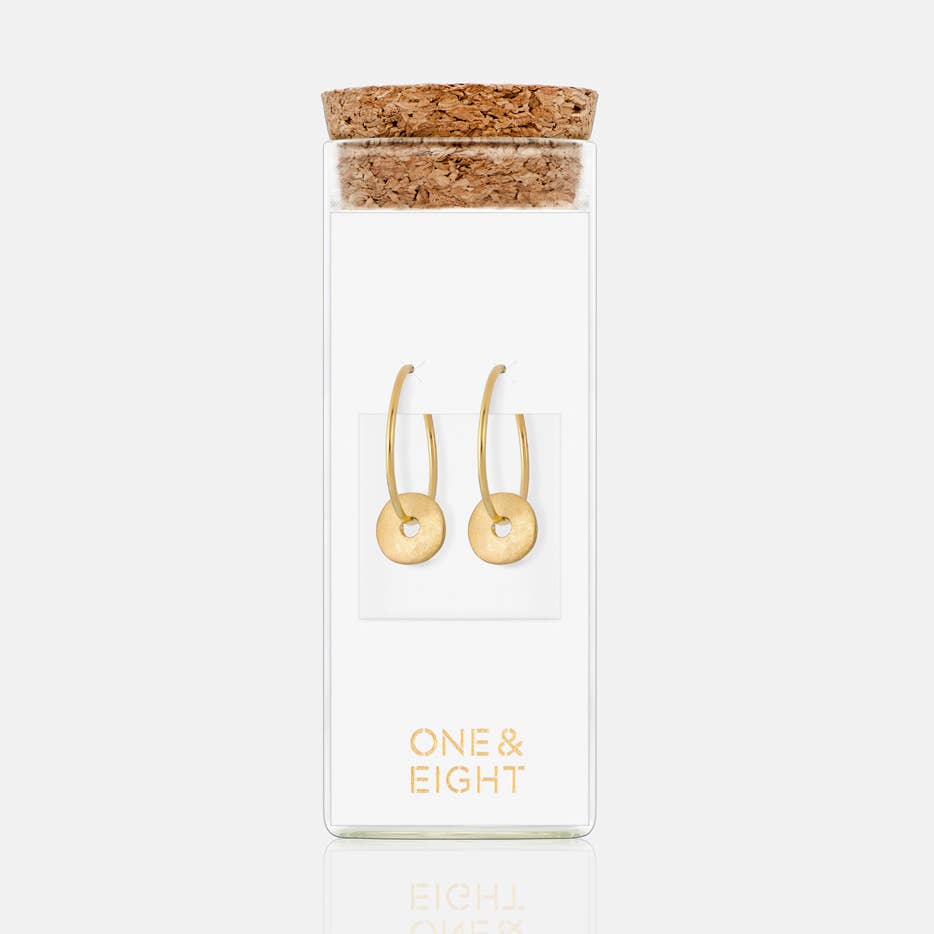 Gold hoop earrings in a clear packaging with cork lid on a white background