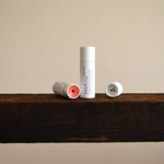 Vely tinted lip balm tubes on a wooden shelf with a neutral background