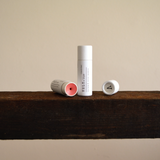 Vely tinted lip balm tubes on a wooden shelf with a neutral background