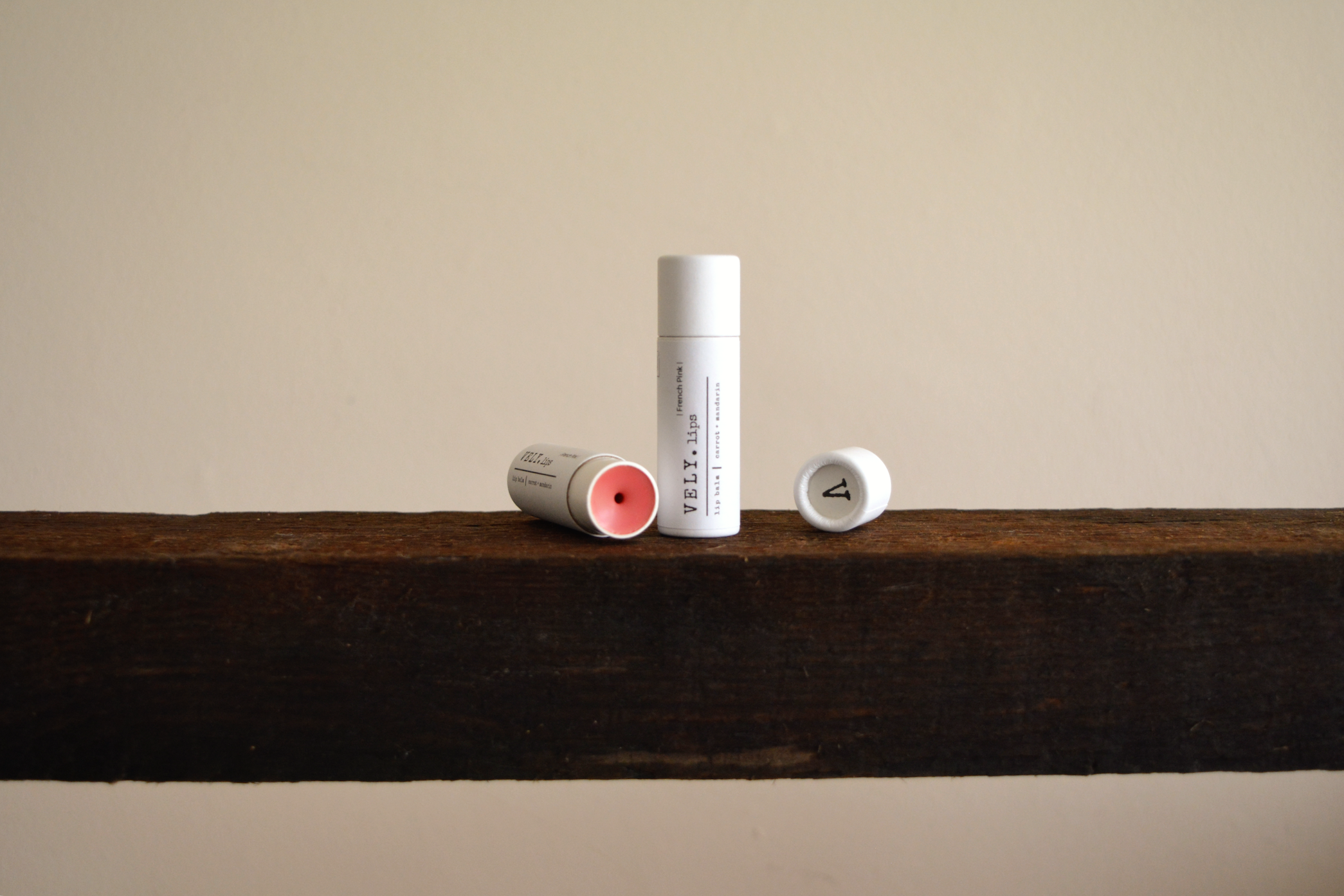 Vely tinted lip balm tubes on a wooden shelf with a neutral background