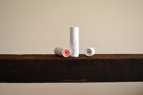 Vely tinted lip balm tubes on a wooden shelf with a neutral background