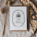 Mother's Day Greeting card with floral design and text. Printed on seed paper. Placed on a textured surface with dried plants and scissors.