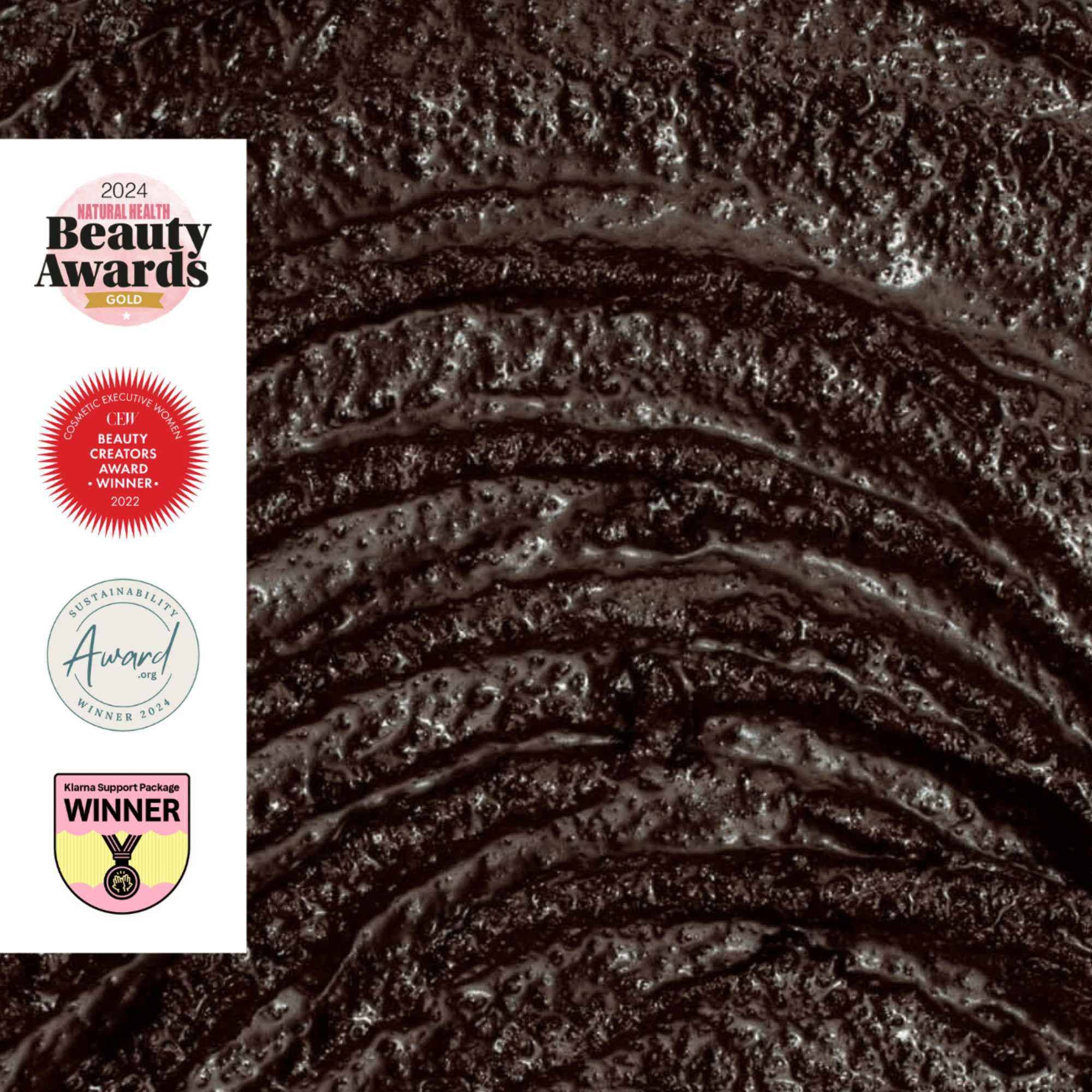 Close-up of dark brown coffee face scrub with 2024 Beauty Awards logos on the left.