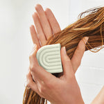 Person holding a Kitsch Conditioner Bar with wet hair against a light background