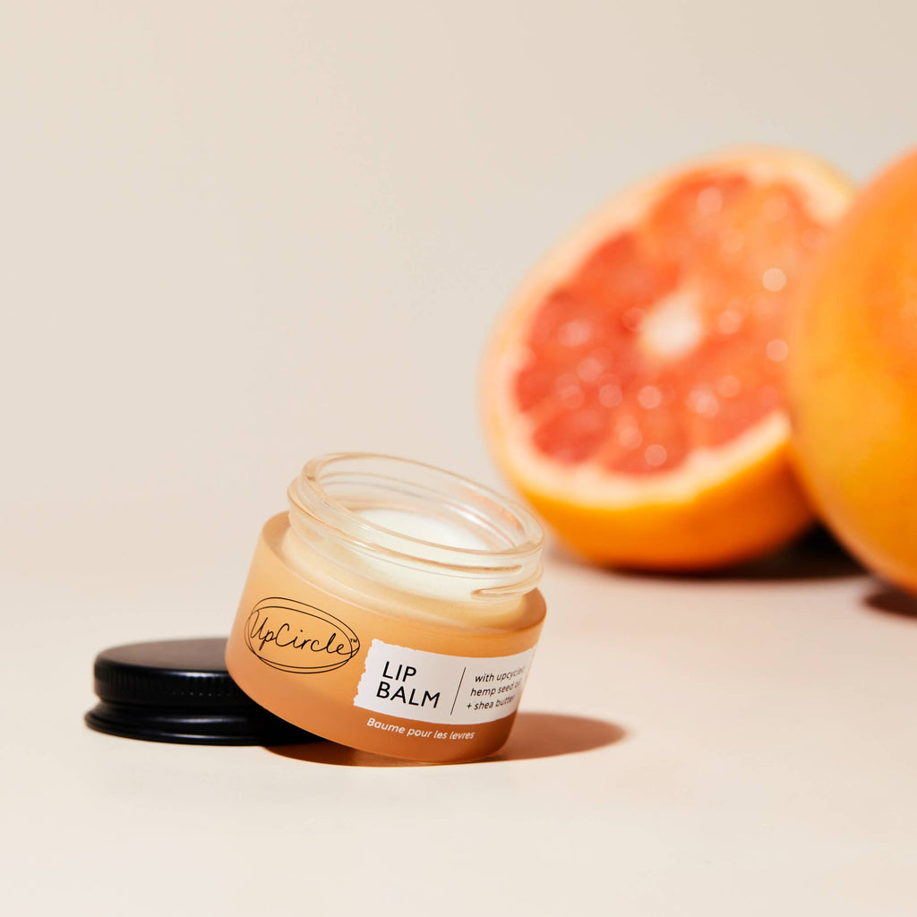 Jar ofUpCircle lip balm with a half-cut grapefruit on a neutral background