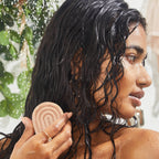 Woman with wet hair holding a bar of Kitsch Strengthening Bond Repair Solid Hair Mask under running water