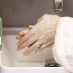 Person washing hands with UpCircle Hand and Body Wash under running water in a sink.
