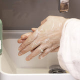 Person washing hands with UpCircle Hand and Body Wash under running water in a sink.