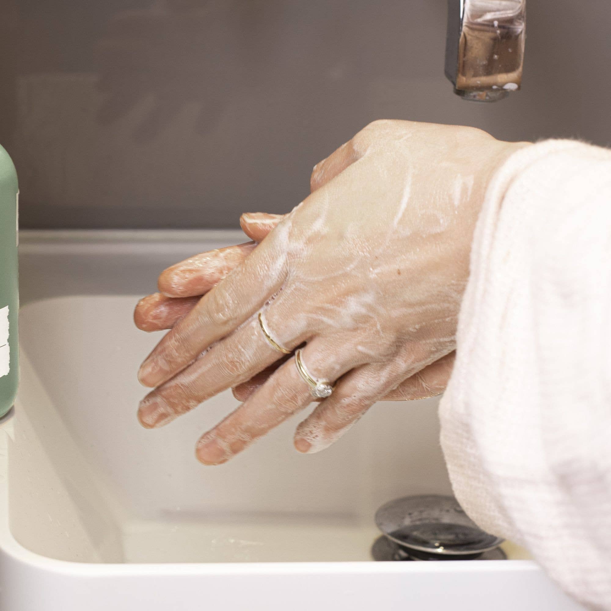 Person washing hands with UpCircle Hand and Body Wash under running water in a sink.