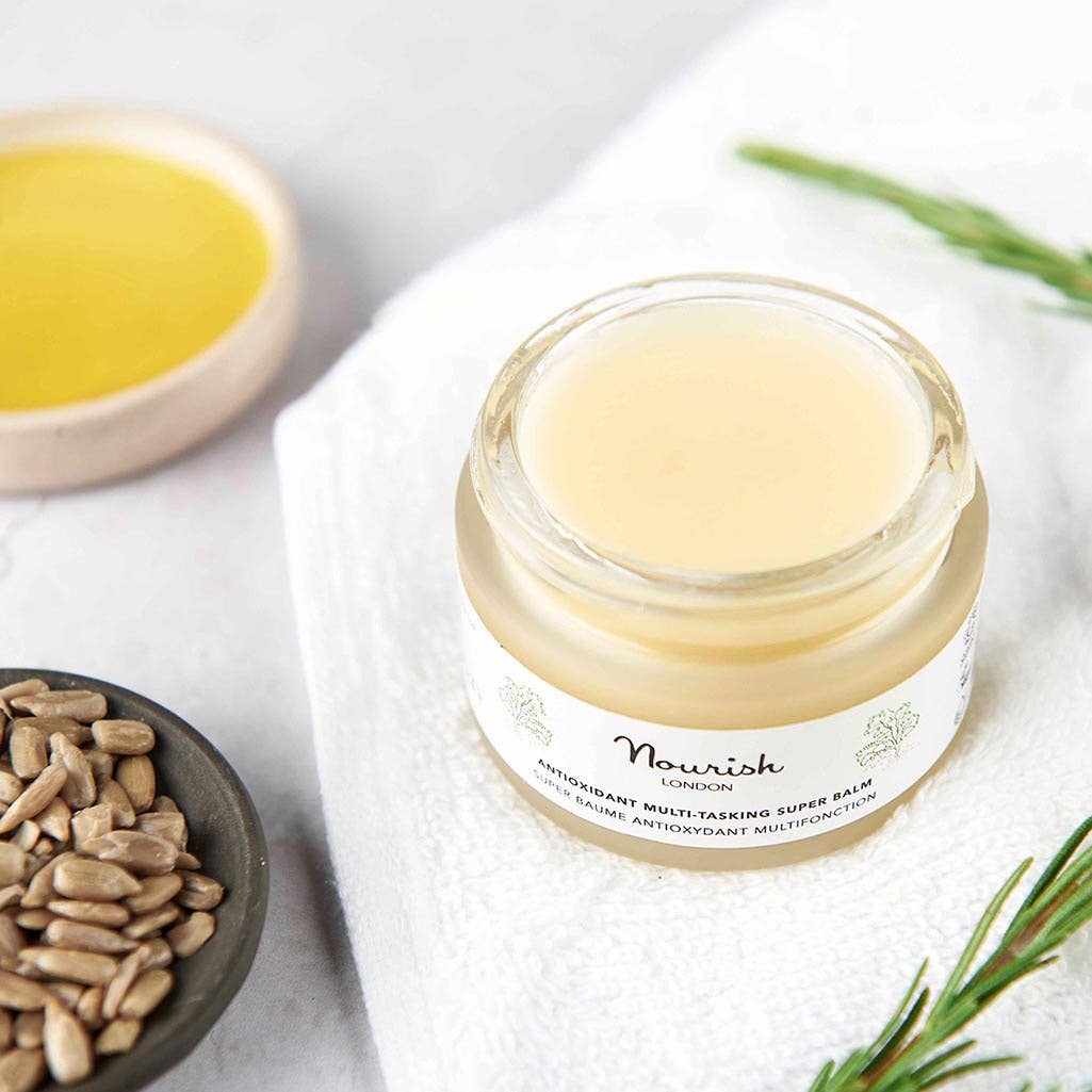 Jar of Nourish lip balm on a white towel with seeds and rosemary leaves.
