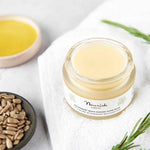 Jar of Nourish lip balm on a white towel with seeds and rosemary leaves.