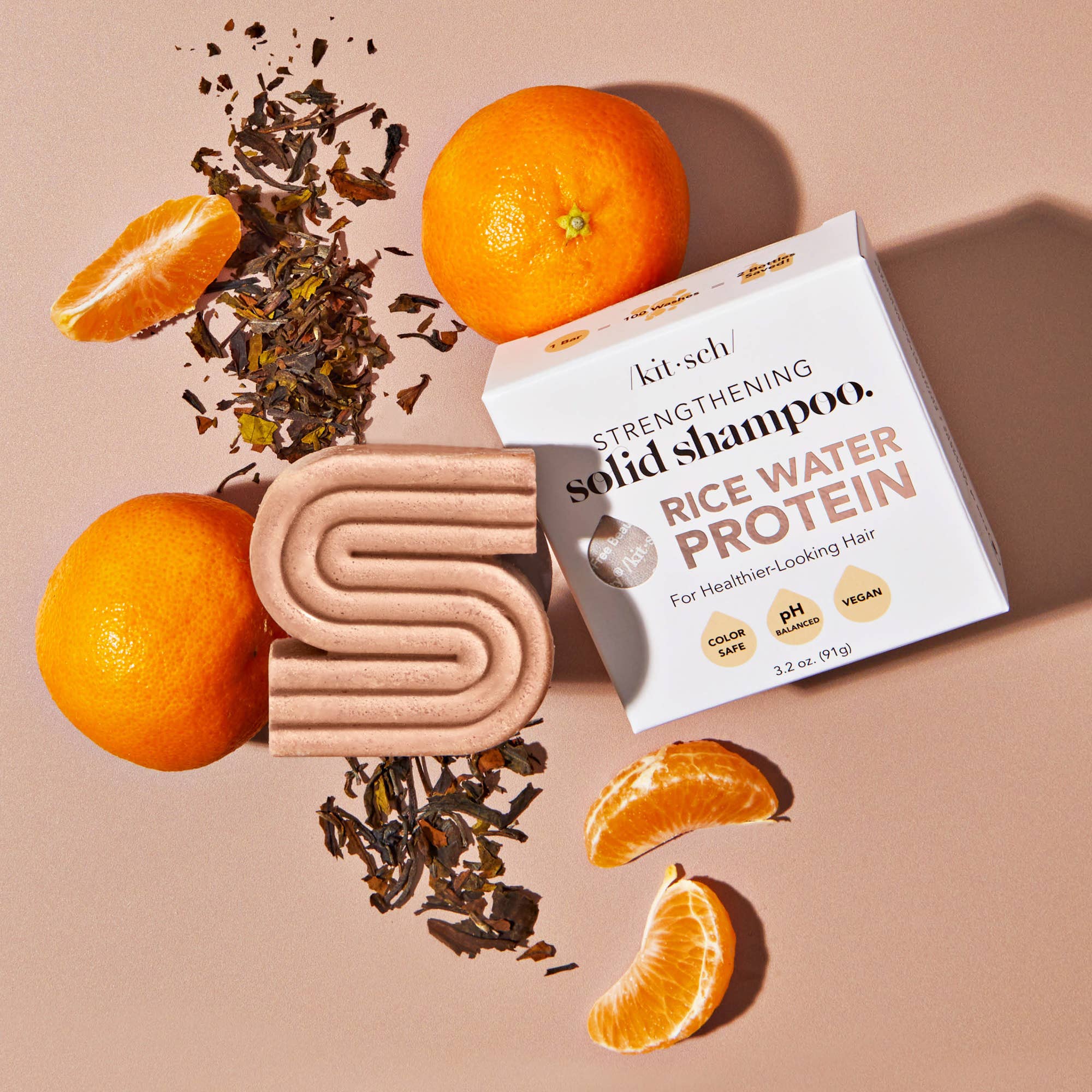 Kitsch Rice Water Protein solid shampoo bar and packaging with oranges and tea leaves on a beige background