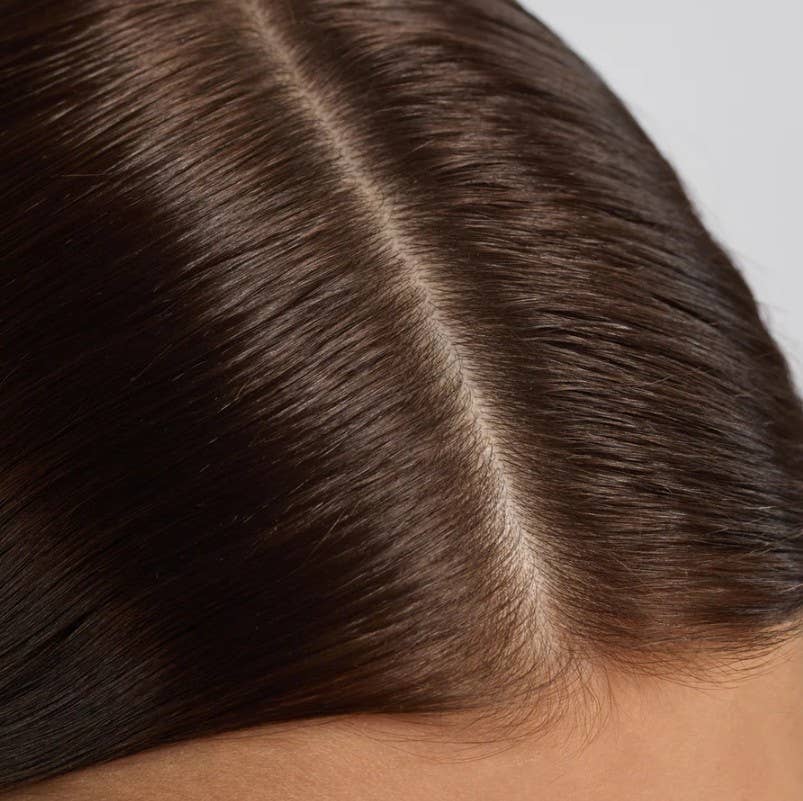 Close-up of a person's healthy scalp and dark, shiny, healthy hair and a visible part line.