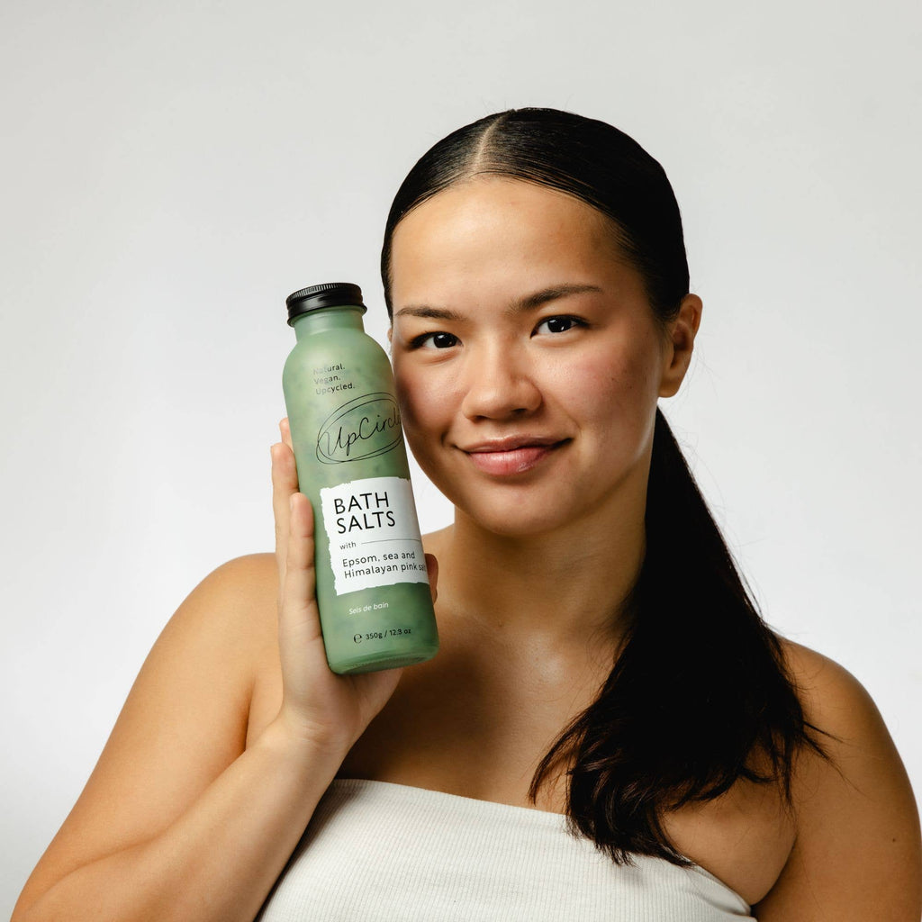 Woman holding a bottle of UpCircle bath salts with a plain background
