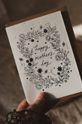 Hand holding a card with 'Happy Mother's Day' text and floral design.