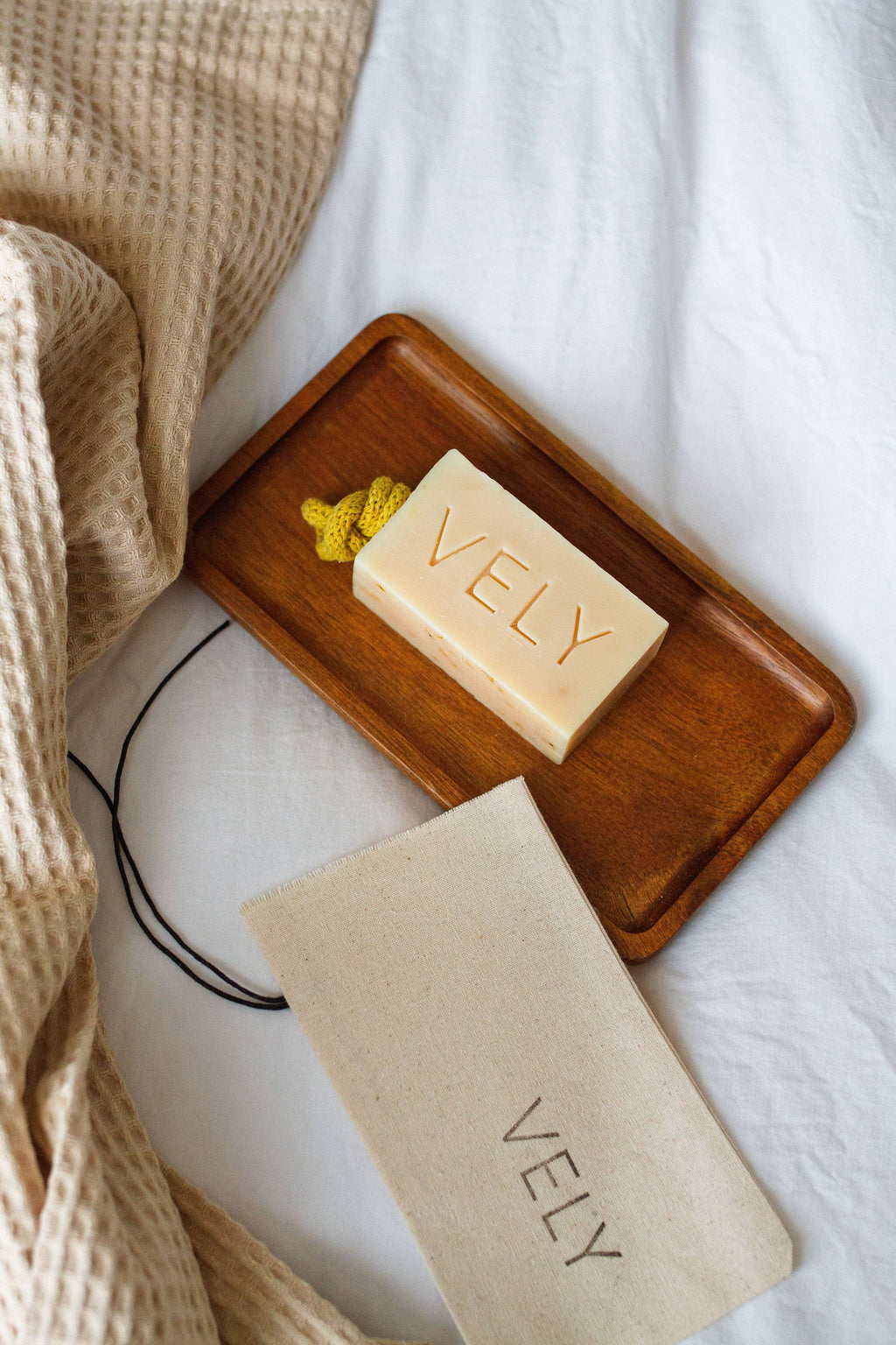 Bar of VELY soap on a wooden tray with a matching soap bag on a white background