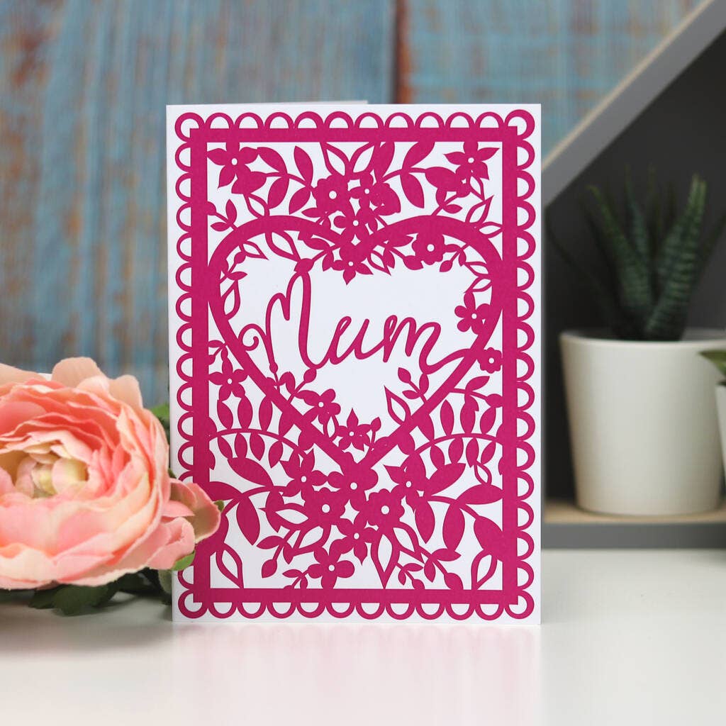 Pink laser-cut card with 'Mum' and floral design next to a pink flower on a white surface.