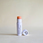pink tinted Vely lip balm with cap in white papckaging on a beige background