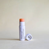 pink tinted Vely lip balm with cap in white papckaging on a beige background