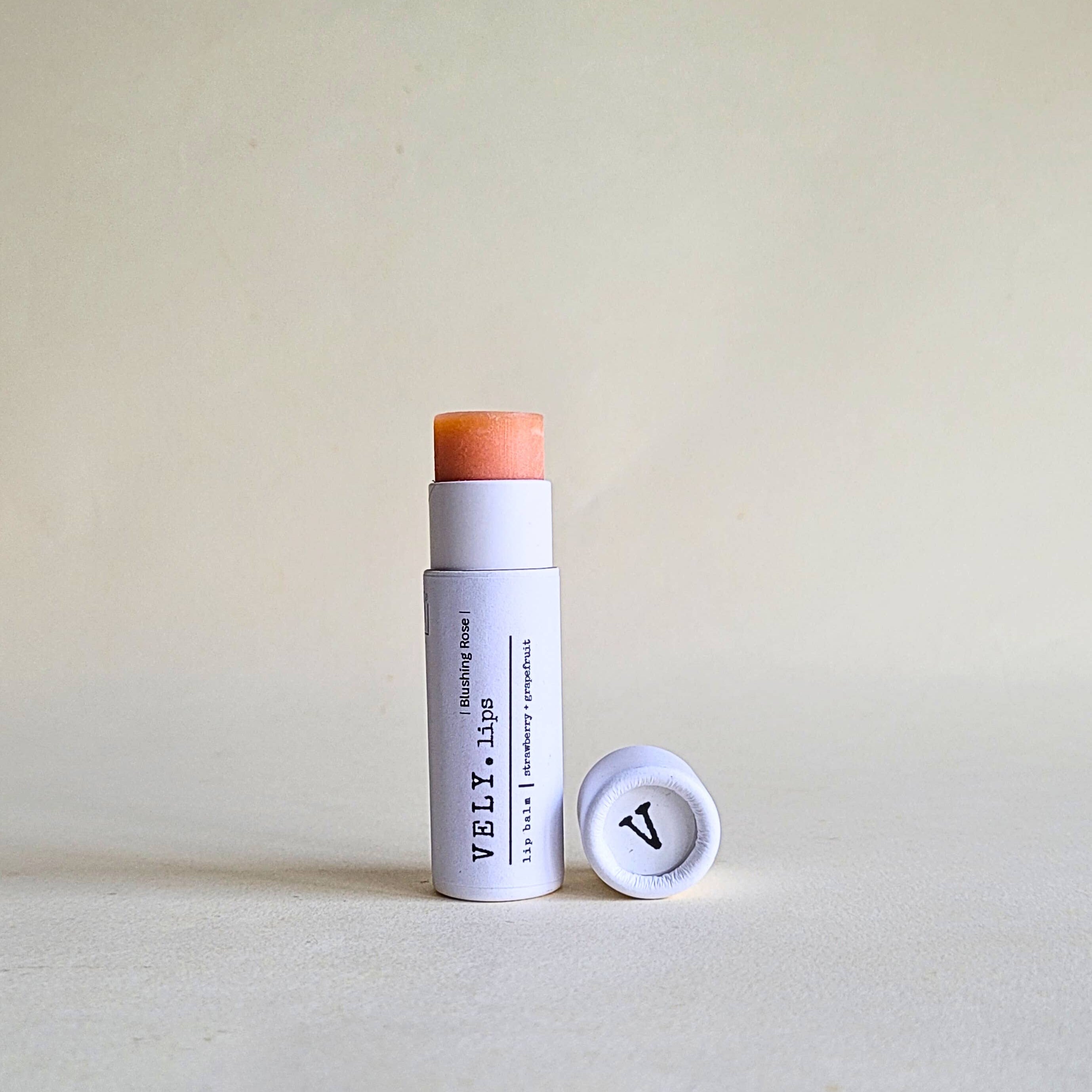 pink tinted Vely lip balm with cap in white papckaging on a beige background