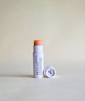 pink tinted Vely lip balm with cap in white papckaging on a beige background