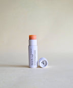 pink tinted Vely lip balm with cap in white papckaging on a beige background