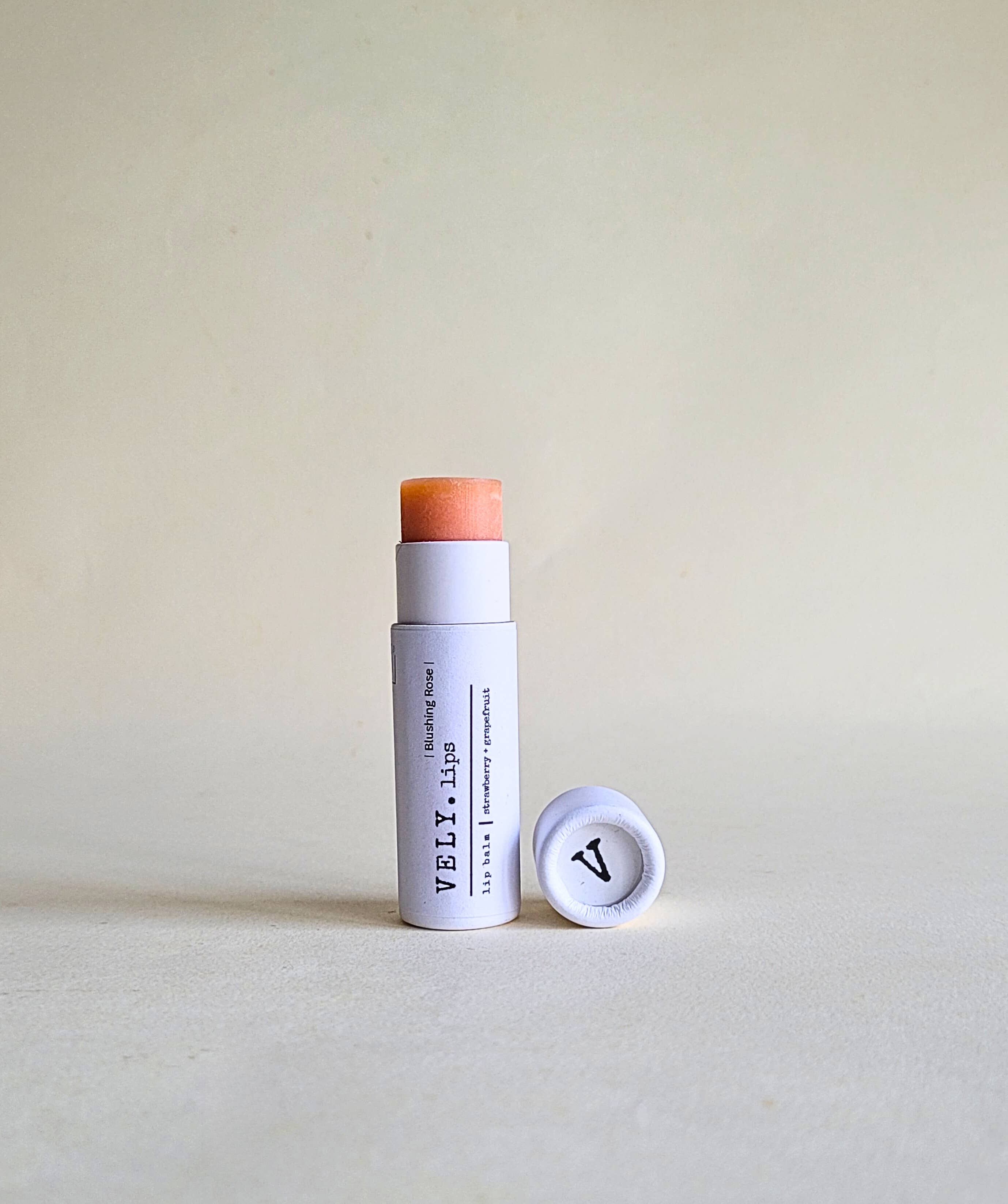 pink tinted Vely lip balm with cap in white papckaging on a beige background