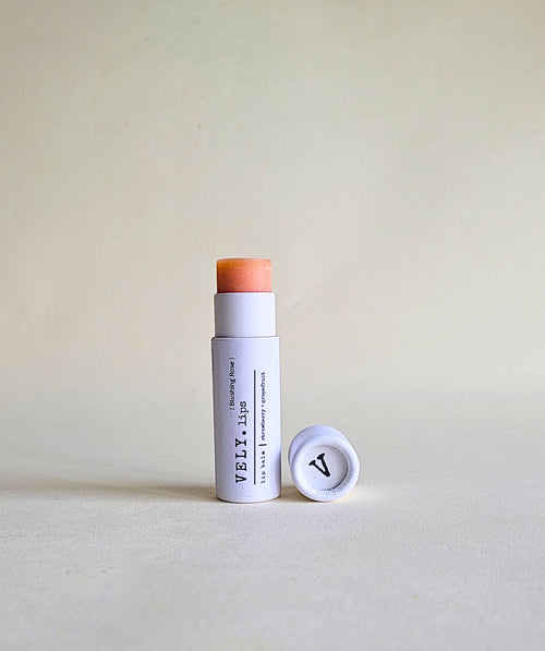 pink tinted Vely lip balm with cap in white papckaging on a beige background