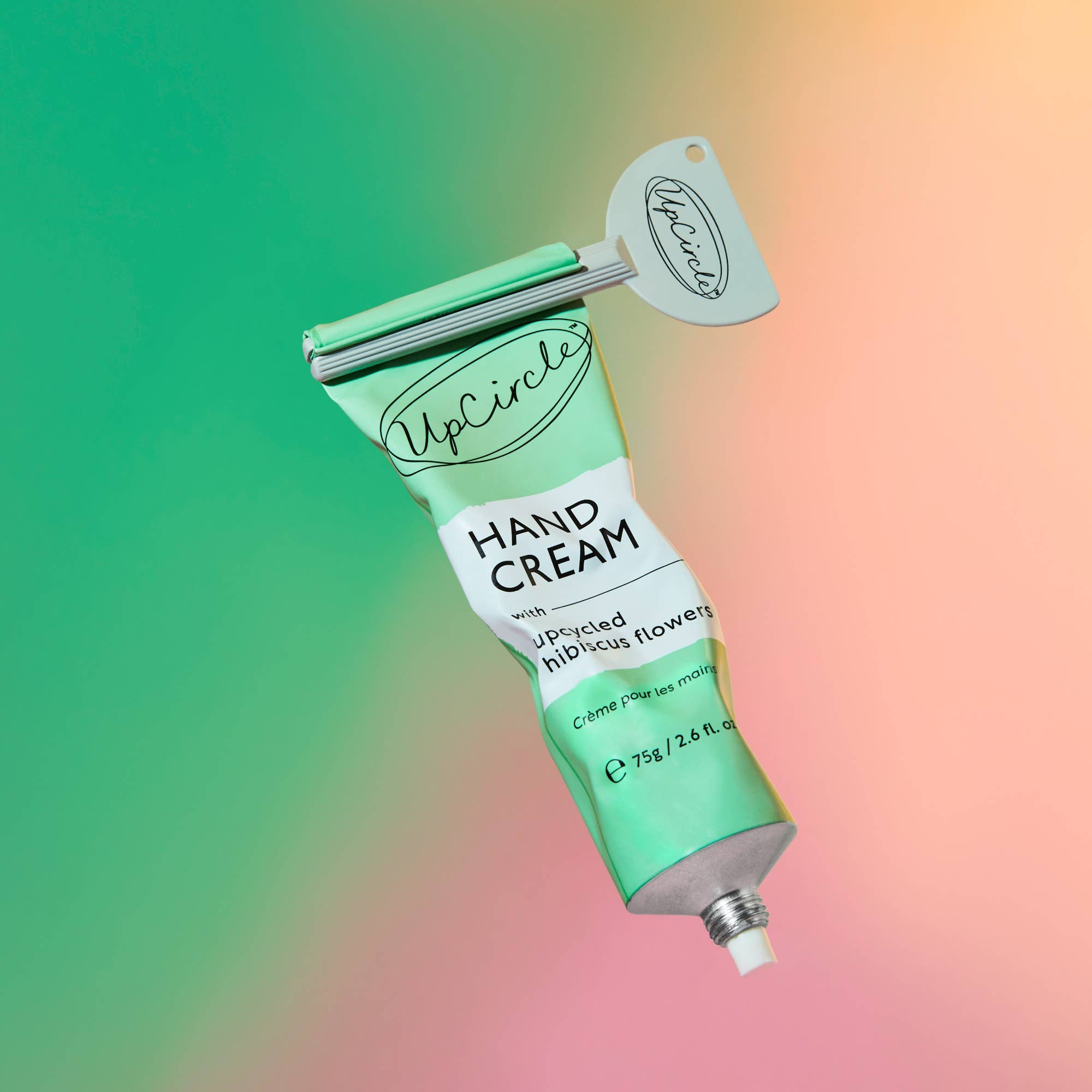 Green tube of Upcircle hand cream with a grey tube squeezer on a colorful gradient background