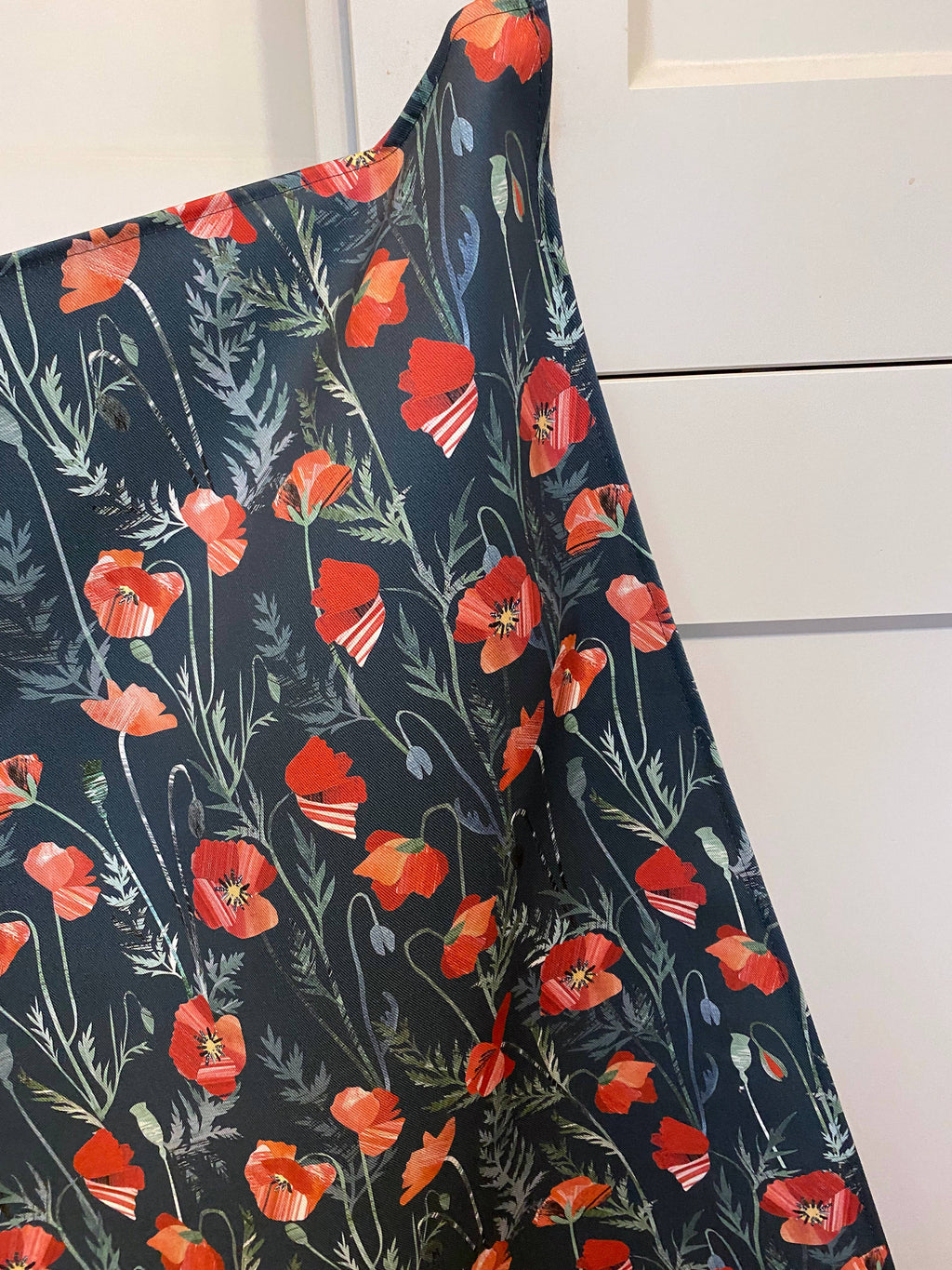 Hanging teatowel with red floral poppy pattern on a dark background draped over a white surface.
