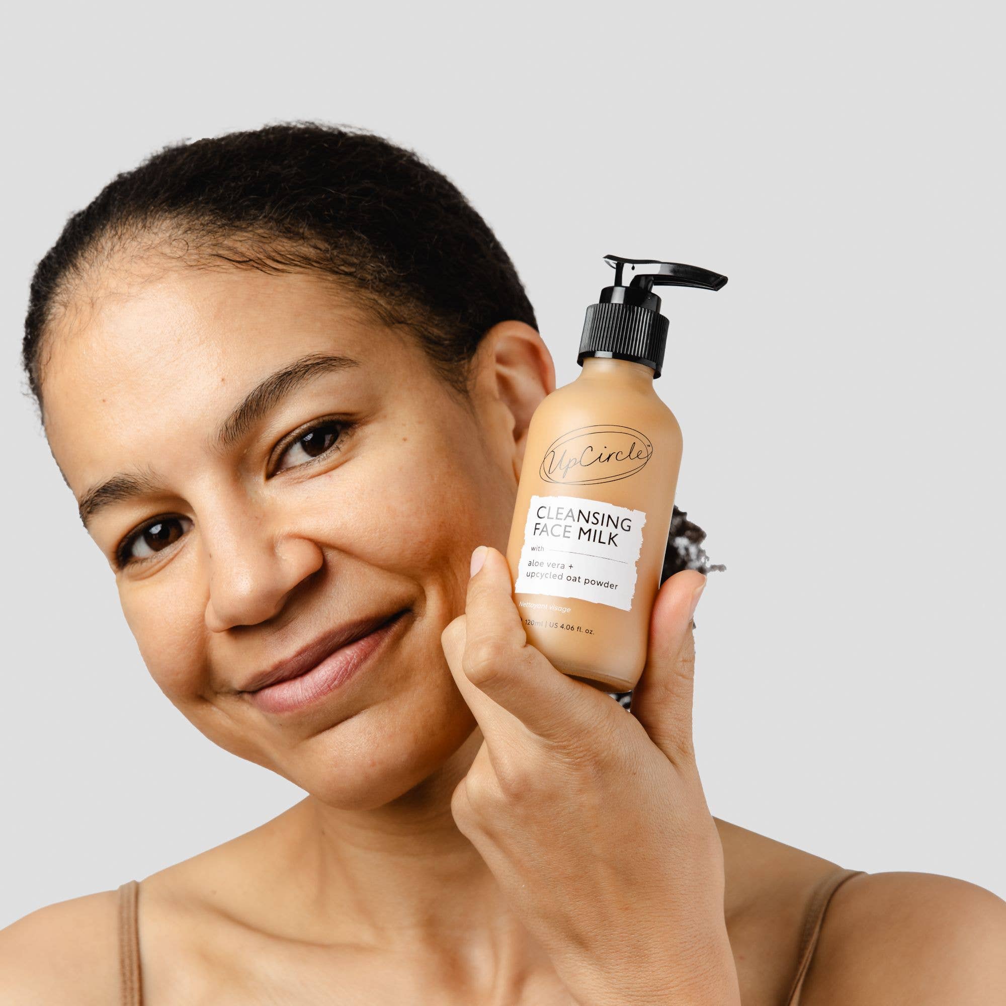 Woman holding a bottle of UpCircle Cleansing Face Milk with a neutral background