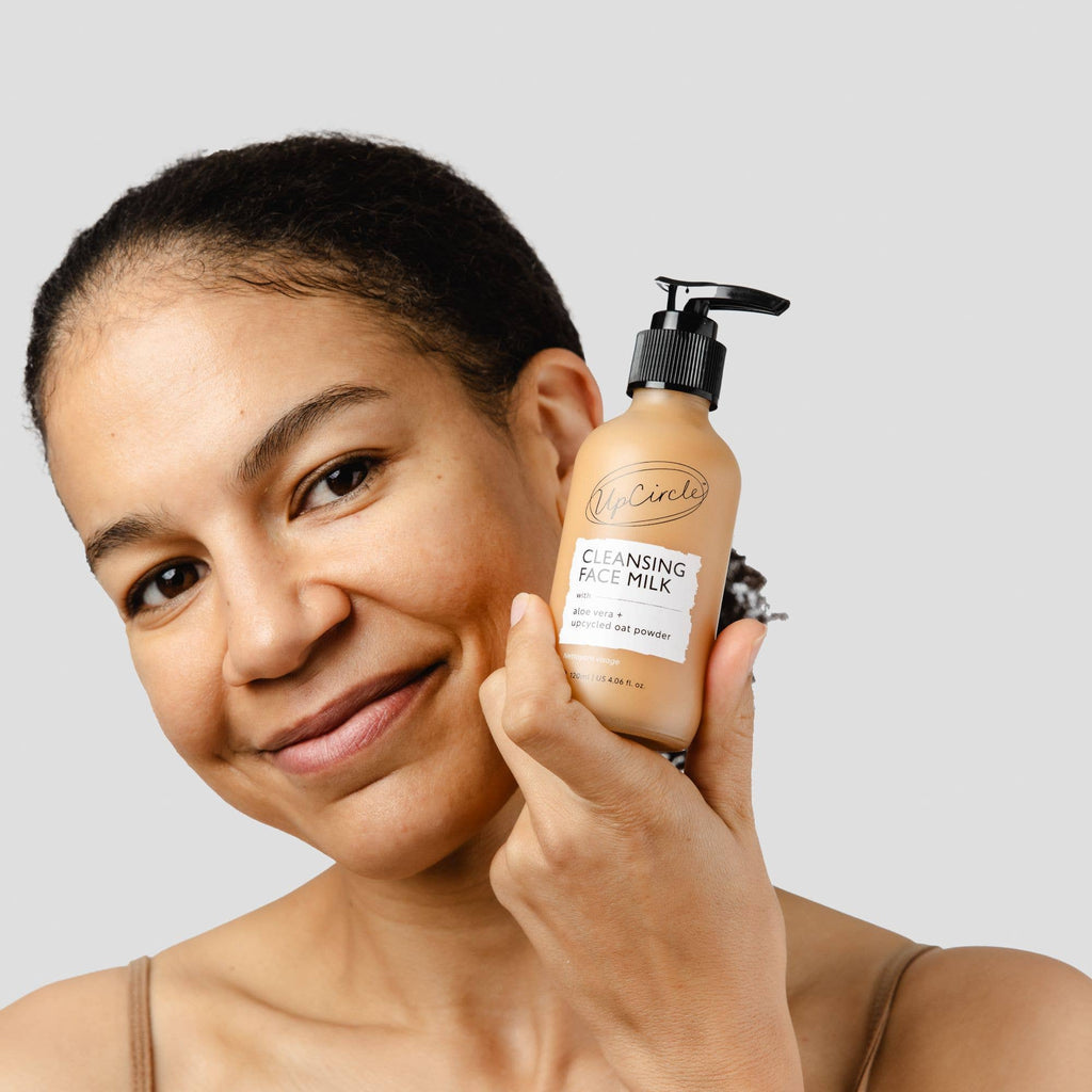 Woman holding a bottle of UpCircle Cleansing Face Milk with a neutral background