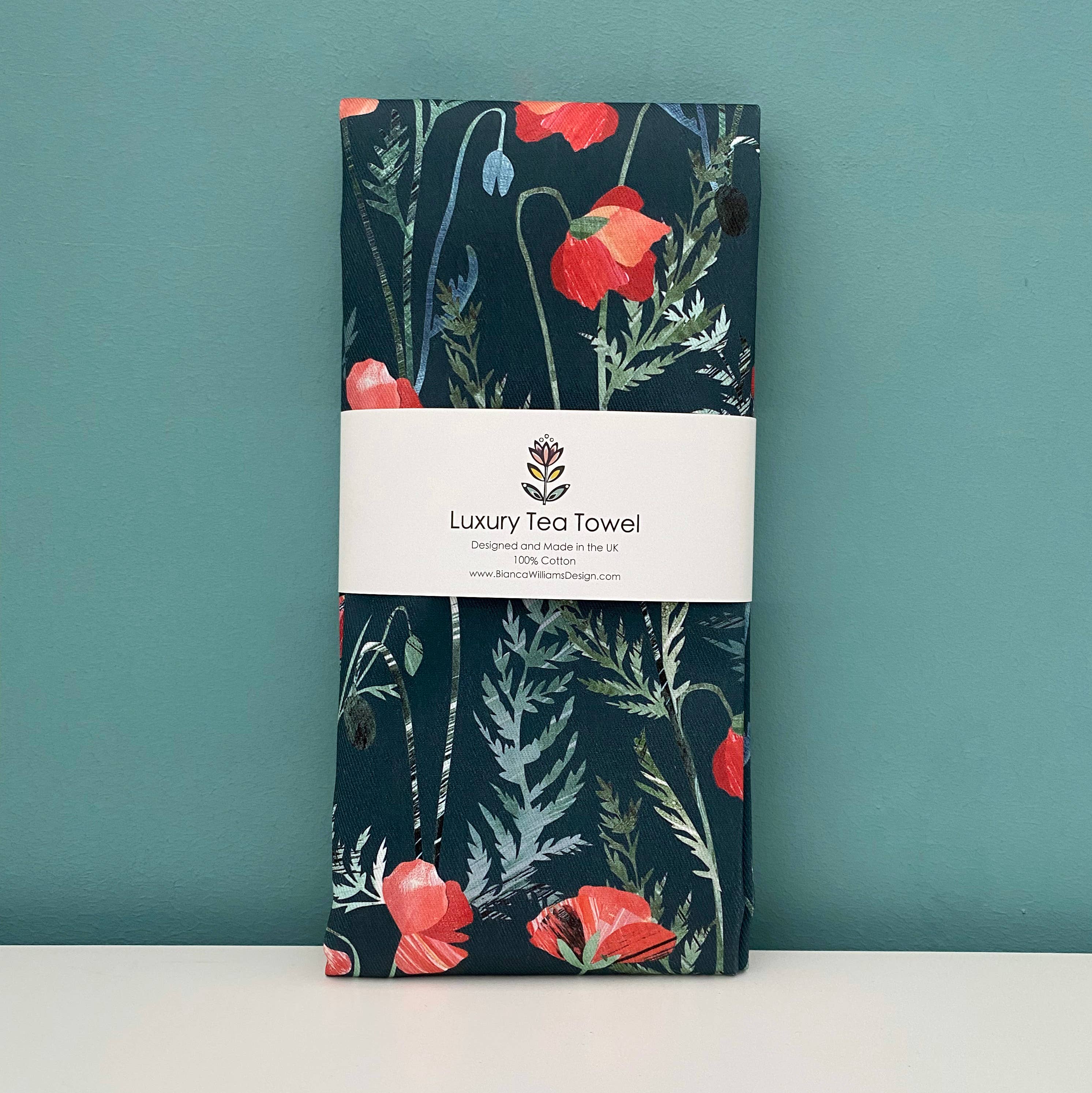 Floral poppy patterned tea towel with a visible brand label on a teal background