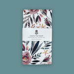 Floral patterned organic cotton tea towel with a brand label on a teal background