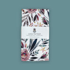 Floral patterned organic cotton tea towel with a brand label on a teal background