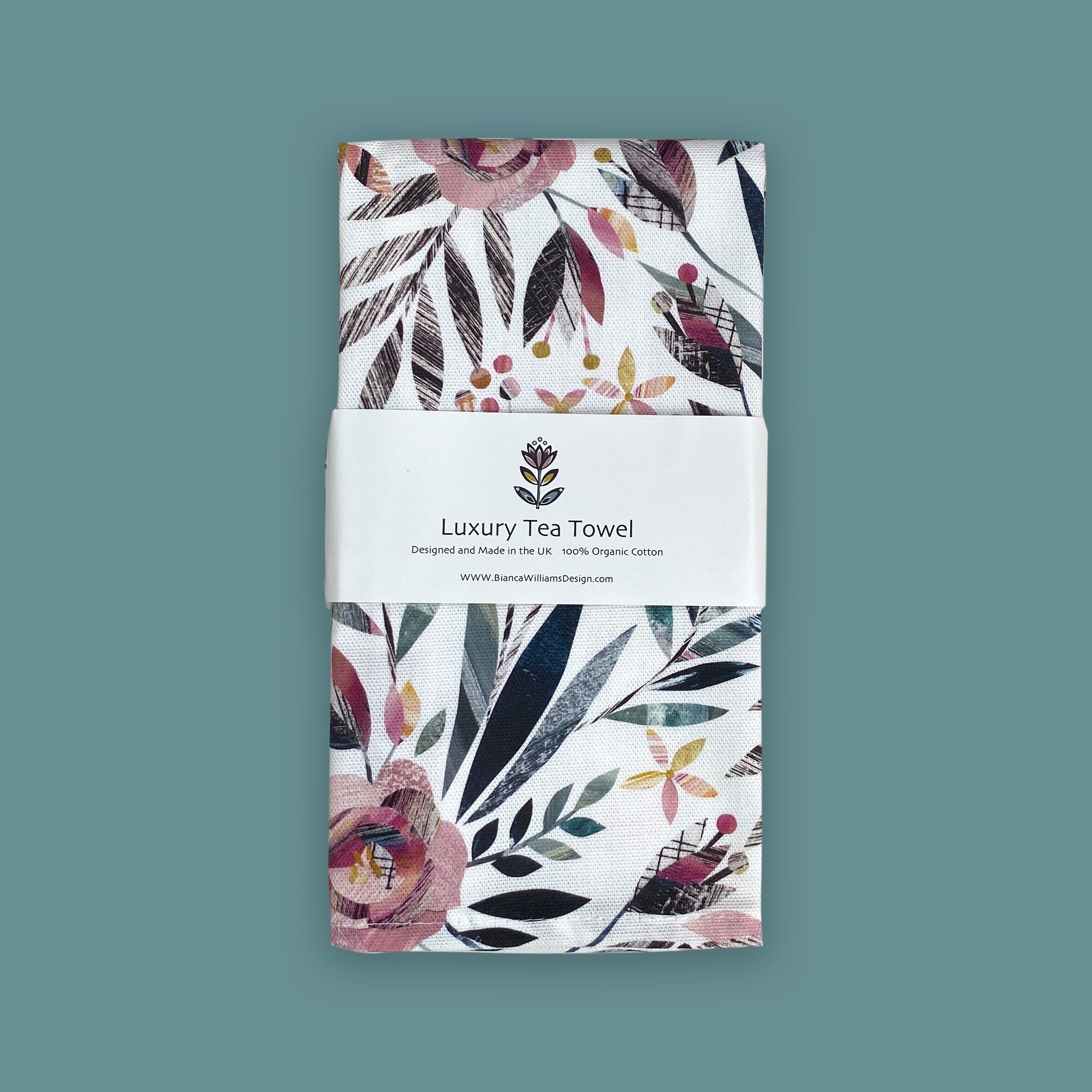 Floral patterned organic cotton tea towel with a brand label on a teal background