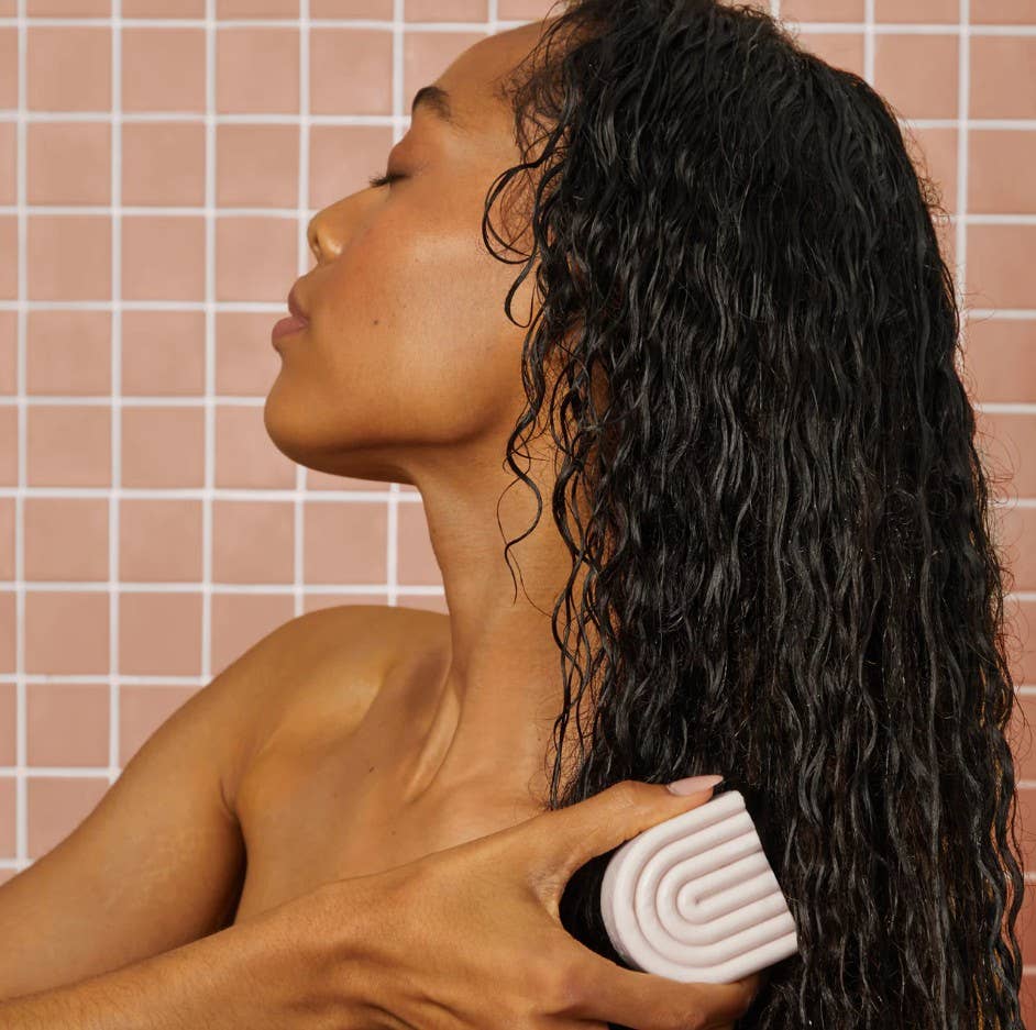 Woman with wet hair using a Kitsch Argan Oil Conditioner Bar, against a tiled wall background