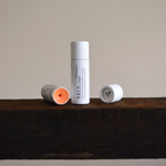 Two Vely tinted lip balm tubes on a wooden surface with a neutral background